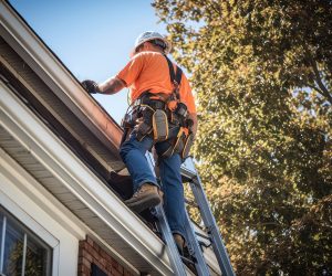 Construction worker on a ladder working on house roof maintenanc